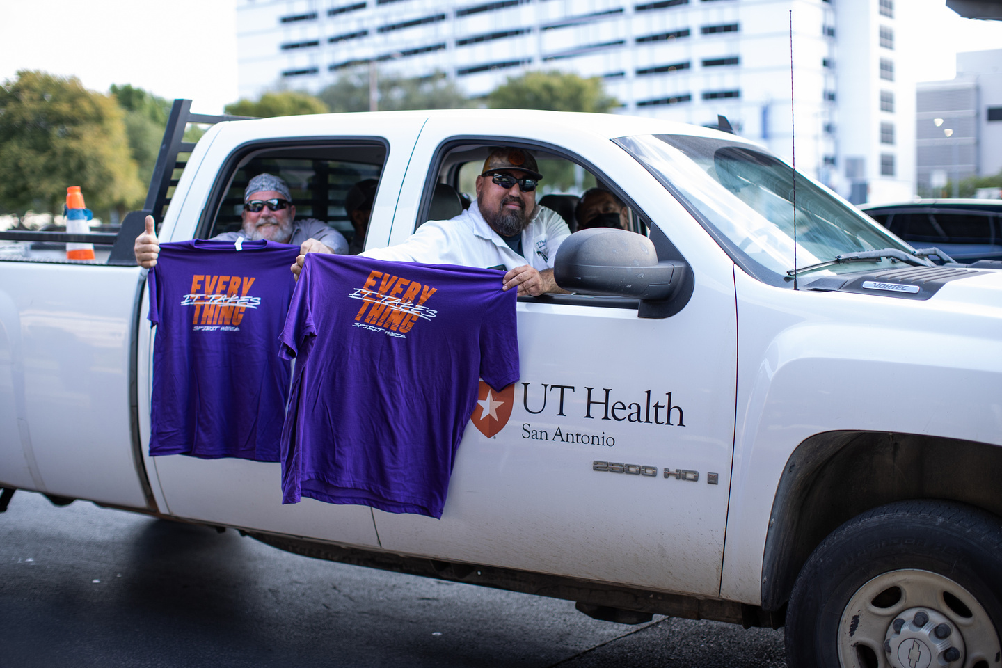 Two male employees holding shirts hanging out of a truck.