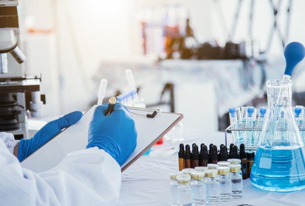 research wearing gloves and writing on clipboard in a lab with test tubes